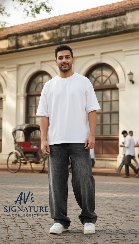 A male model in a white oversized t-shirt and AV's Signature Collection charcoal baggy jeans standing on a cobblestone street with a vintage background.